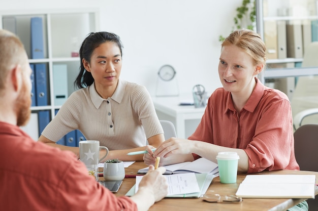 Group of business colleagues sitting at the table and talking to each other during business meeting at office