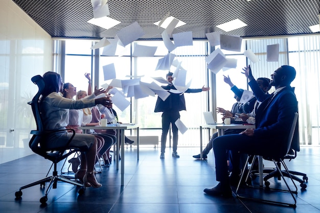 Group of business people rejoicing in closing the quarter successfully tossing up paper documents in the modern office panoramic window