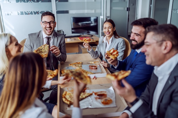 Group of business people sitting in boardroom, chatting, laughing and having pizza for lunch.