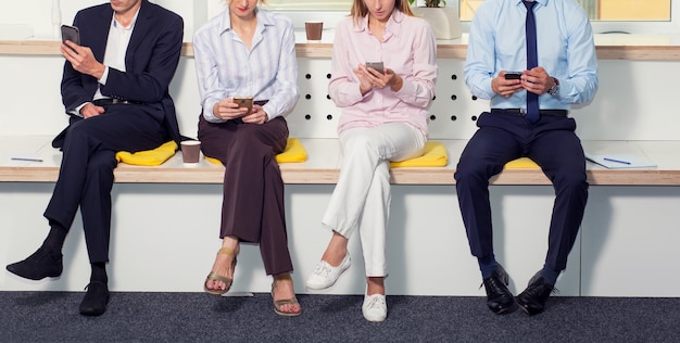 Group of business people, without faces, using smartphones while sitting in the office.