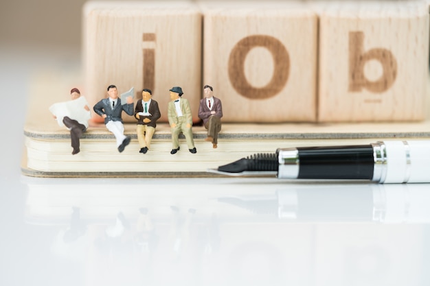 Group of business team sitting on notebook with pen and job word from wooden blocks.