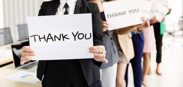 Group of businesspeople join together greeting and hold thank you word for sign of thankfulness to someone in modern office. Idea for good teamwork feeling declaration and support for colleagues.