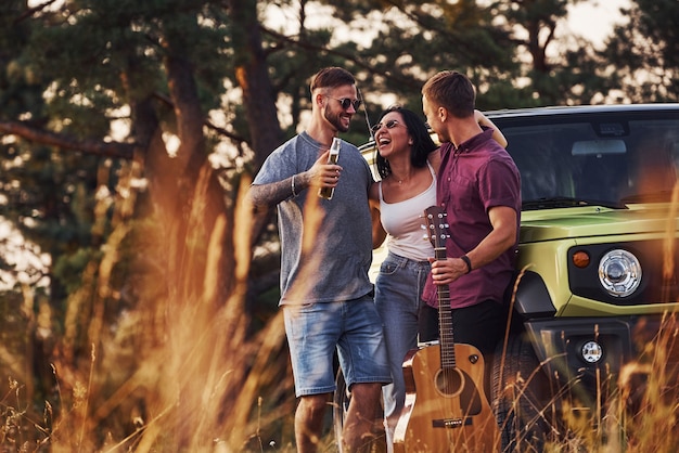 Group of cheerful friends have nice weekend at sunny day near theirs green car outdoors