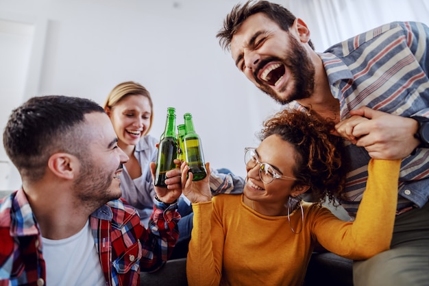 Group of cheerful friends having fun at home, toasting with beer and laughing.