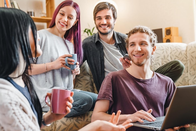 Group of cheerful friends having fun while looking at photos on laptop together