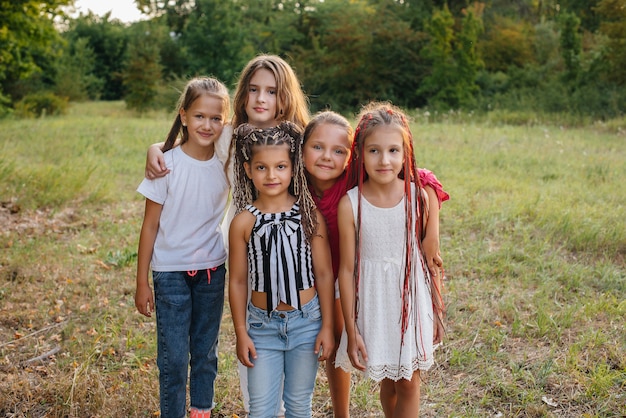 A group of cheerful girls are smiling and playing in the Park during sunset. Children's summer camp.