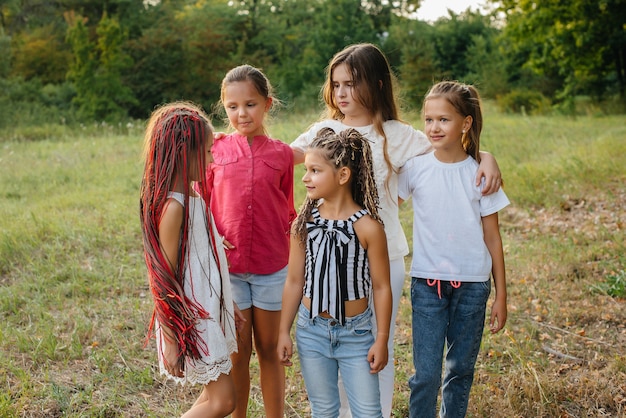 A group of cheerful girls are smiling and playing in the Park during sunset. Children's summer camp.