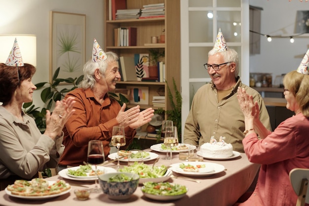 Group of cheerful senior people clapping hands while looking at their friend