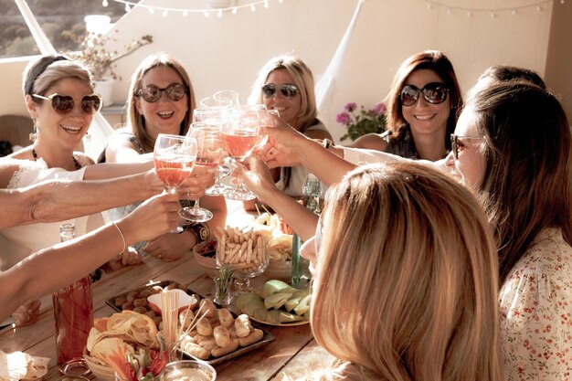 Group of cheerful women in friendship enjoying party for birthday Wooden table Wineglass for celebrate and large smiles Nine people