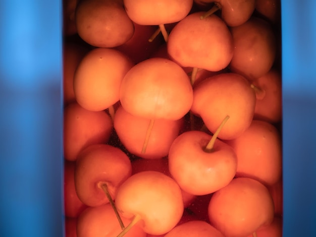 Group of cherries placed in a glass container and covered with pomace alcohol to make the tasty sour cherries and the appreciated pomace of sour cherries liquor and a blue background