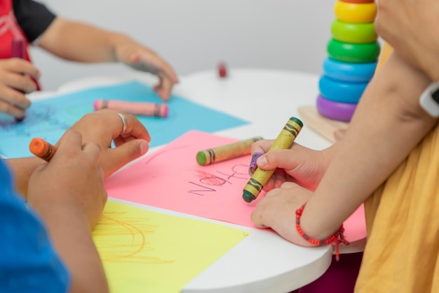 Group of children drawing on colored sheets with crayons on a white table