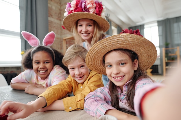 Group of children smiling at camera and making selfie portrait on mobile phone together with their teacher