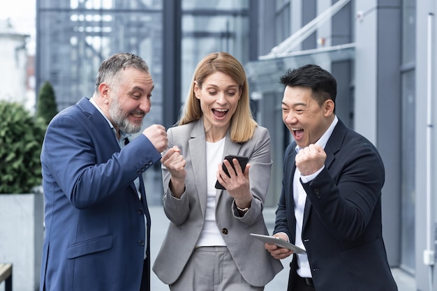 Group of colleagues employees read good news looking at smartphone happy team rejoices about