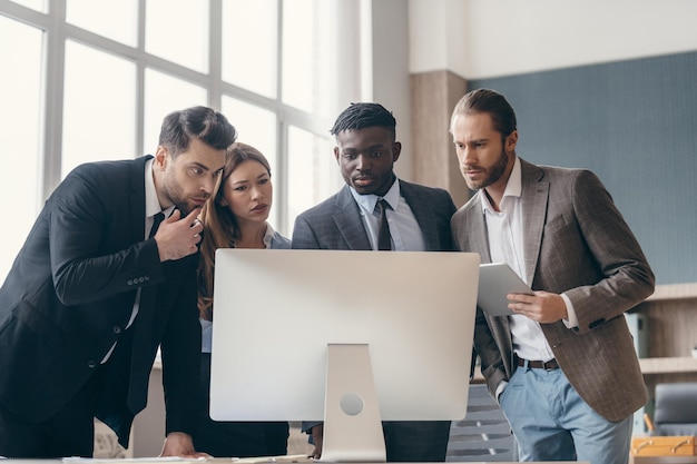 Group of confident business people looking at computer monitor while having meeting in the office