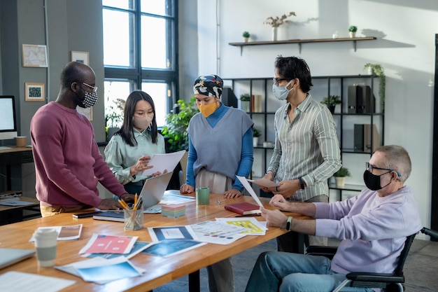 Group of contemporary employees in protective masks discussing documents