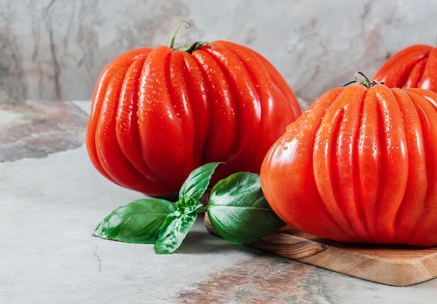 A group of Costoluto big tomatoes with basil on a brown background space for text