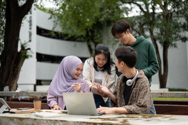 A group of diverse college students is discussing project details using a laptop in a campus park