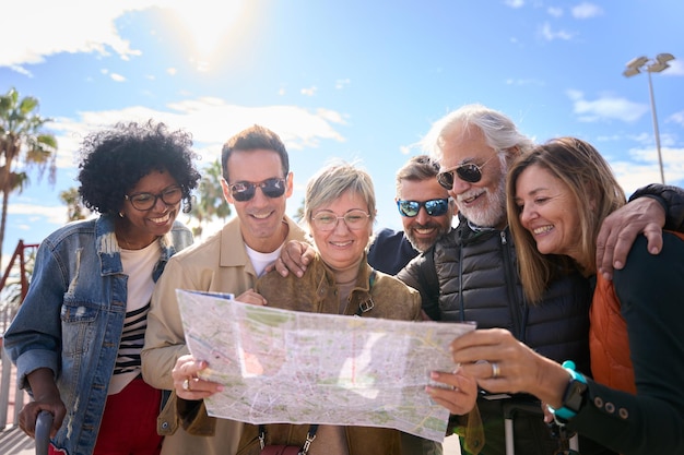 Photo group diverse middleaged tourist people standing looking at travel map in hands on vacation city