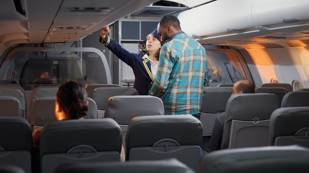 Group of diverse passengers boarding on airplane seats, talking to flight attendant on airline service. Flying and travelling with commercial airline, chatting with stewardess about service.