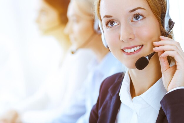 Photo group of diverse phone operators at work in sunny office. handsome business woman with headphones consulting clients. call center and business people concept.