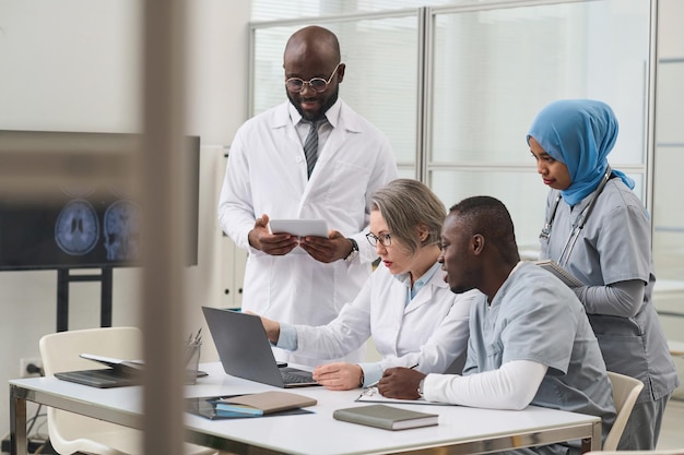 Group of doctors examining xray image online on laptop at table during meeting in office