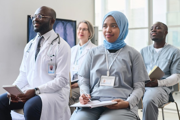 Group of doctors making notes and listening to speaker while sitting at conference