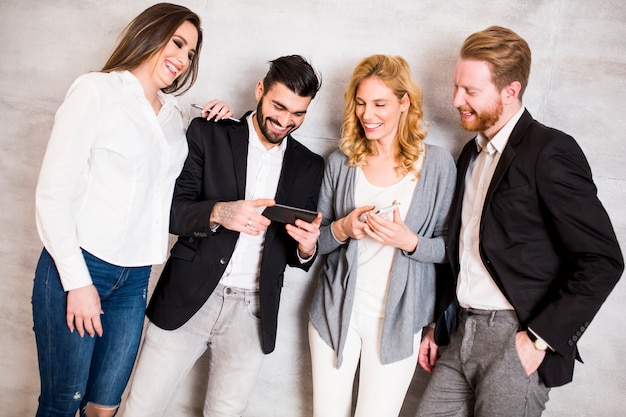 Group of elegant businesspeople standing against the wall and using their mobile phones