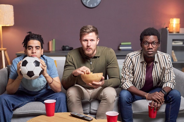 Group of fans watching sports match at home with intense face expression