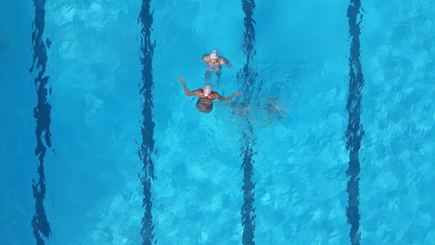 A group of female athlete performs synchronized swimming routines in an outdoor pool as seen from the air