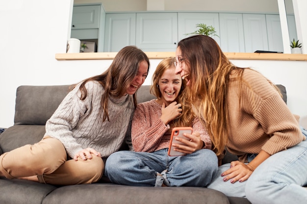 Group of female friends on the sofa at home, using a mobile phone laughing