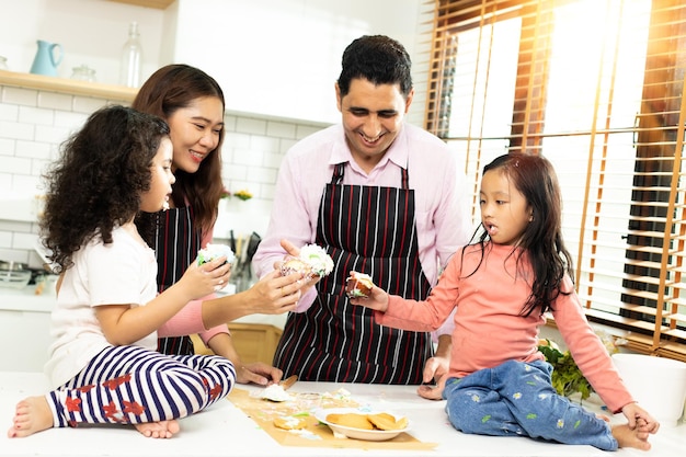 Group of four Diverse Family Asian and Arab Preschool African Arab kid person make Cake cooking in kitchen Father Mother prepare decoration pretty with fun educate Cream mess over face copy space