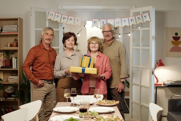 Group of four happy senior friends with packed giftboxes looking at camera