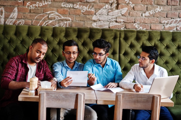 Group of four south asian mens posed at business meeting in cafe Indians together and sign important documents Contract to study and work