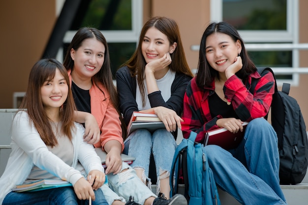 Group of four young attractive asian girls college students studying together in university campus outdoor looking at camera. Concept for education, friendship and college students life.