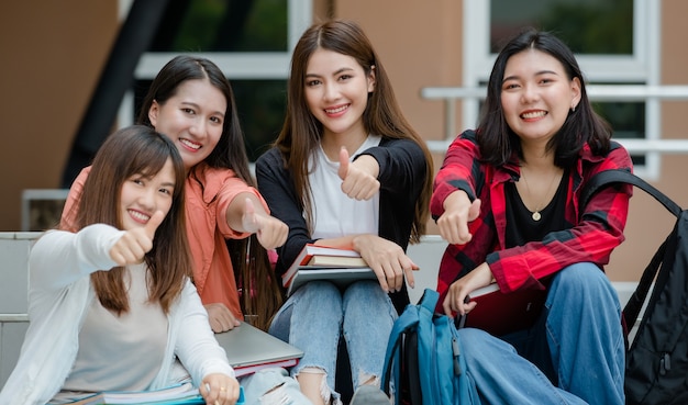 Group of four young attractive asian girls college students studying together in university campus outdoor looking at camera. Concept for education, friendship and college students life.