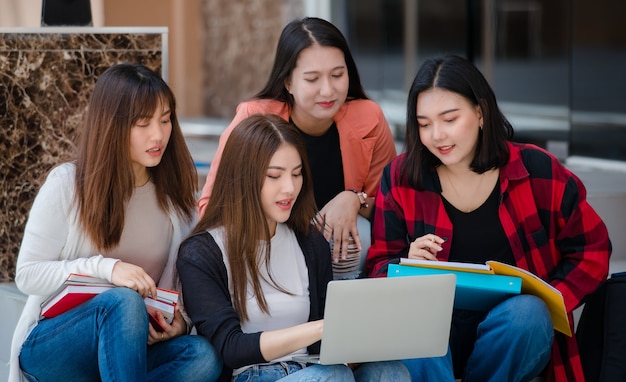 Group of four young attractive asian girls college students studying together using laptop in university campus outdoor. Concept for education, friendship and college students life.