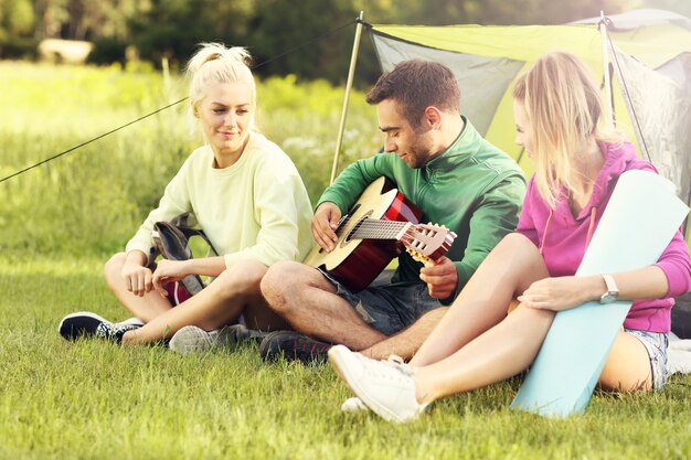 Group of friends camping in forest and playing guitar