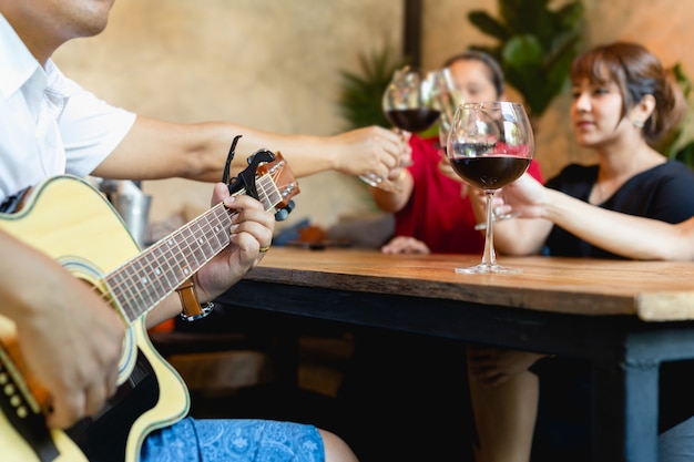 Group of friends celebrating and playing guitar while drinking red wine.