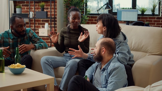 Group of friends enjoying funny conversation at house party, drinking beer from bottles and having fun. People talking about friendship memories and laughing, bonding at hangout.