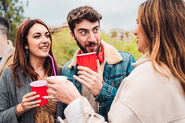 Group of friends get together at the park and drinking beers from red plastic glasses