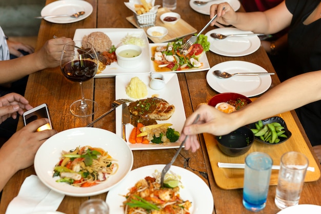 Group of friends hands with fork having fun eating variety food on the table.