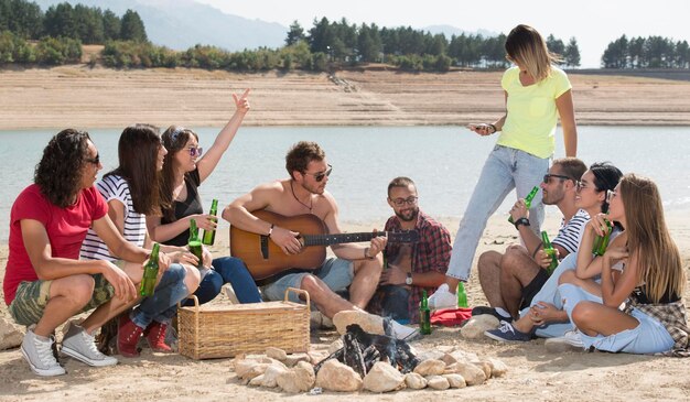 Group of friends having fun making BBQ on bonfire and relaxing by a lake.