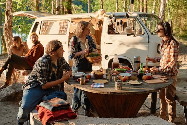 Group of friends having lunch at the table outdoors during their camping on the nature