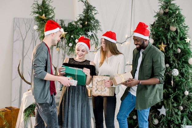 Group of friends laughing and sharing Christmas gifts in beautiful cozy studio