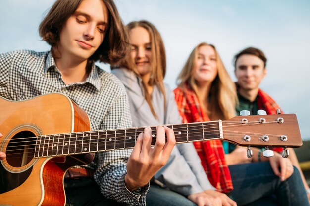 Group of friends listen to busker playing guitar. Musician artistic lifestyle. Teenagers leisure