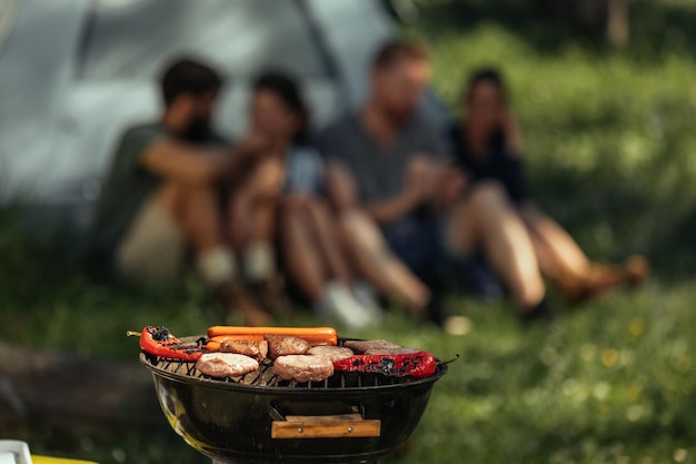 Group of friends making barbecue while camping in the woods