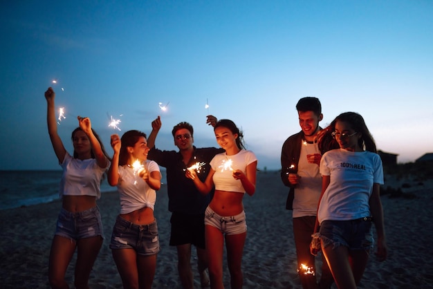 Group of friends at night on the beach with sparklers Young friends enjoying on beach holiday