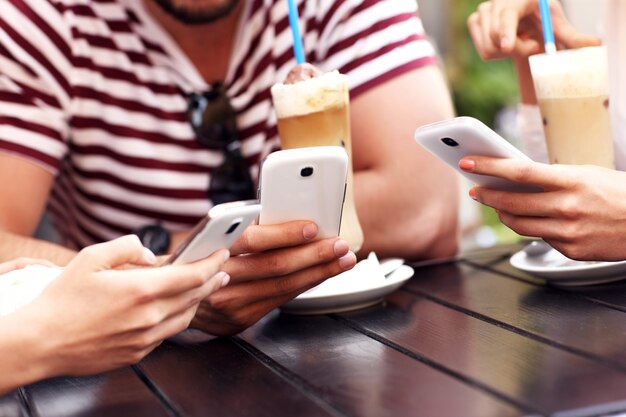 group of friends resting in an outdoor cafe and using smartphones