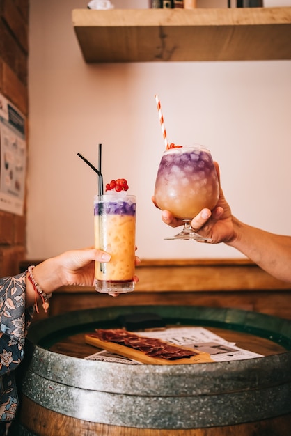 A group of friends sits on the terrace in the summer behind a wooden barrel with cocktails and a snack