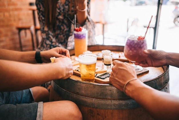 A group of friends sits on the terrace in the summer behind a wooden barrel with cocktails and a snack